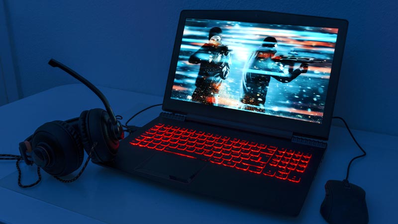 Portátil preto com o teclado iluminado a vermelho e uma imagem de jogo de vídeo num ambiente escuro